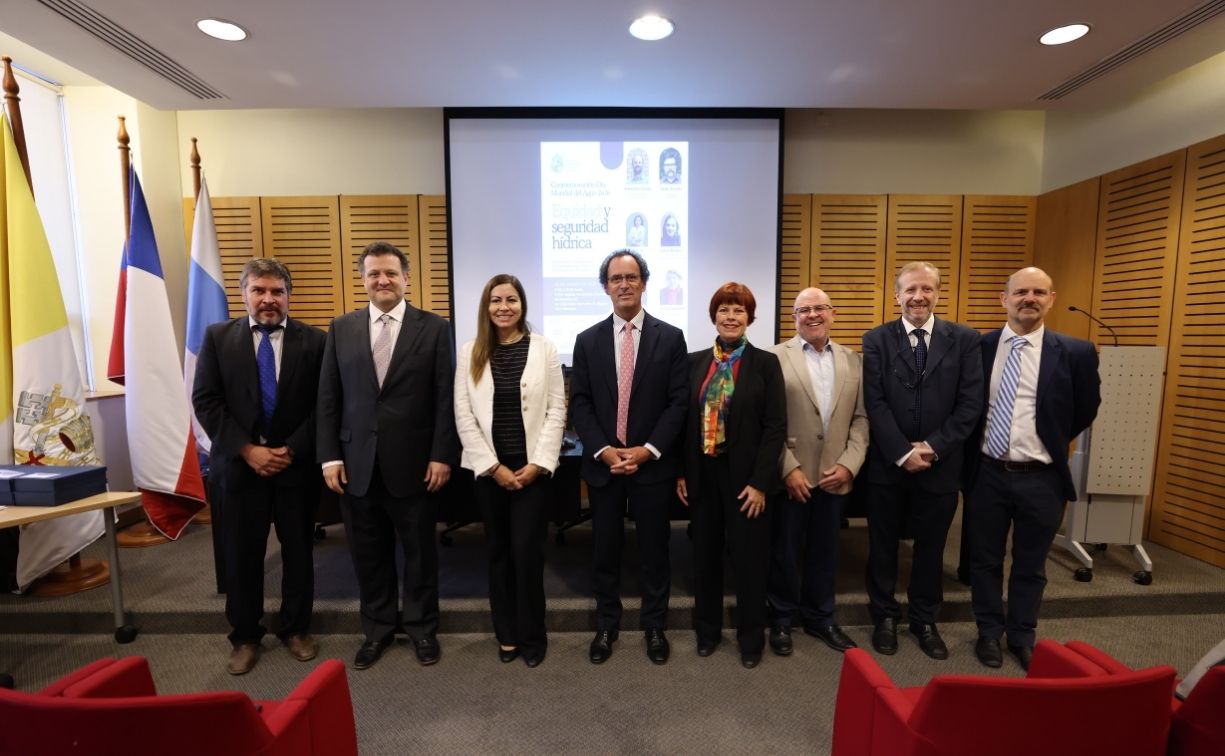 Fotografía de un grupo de personas vestidas formalmente, autoridades y académicos, de pie en un salón, en medio se encuentra el Rector UC