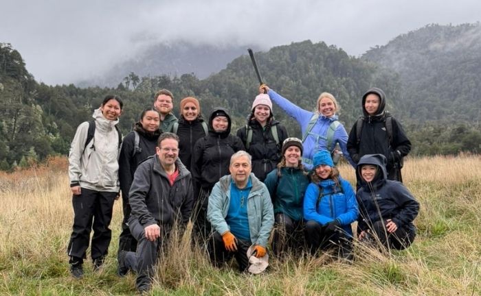 Fotografía de un grupo de personas abrigadas con equipamiento de trekking en un terreno montañoso con neblina