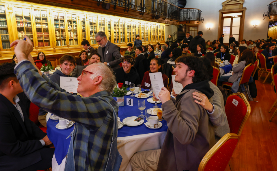 Fotografía de un salón con mesas, un grupo de personas se toma una selfie en una de ellas
